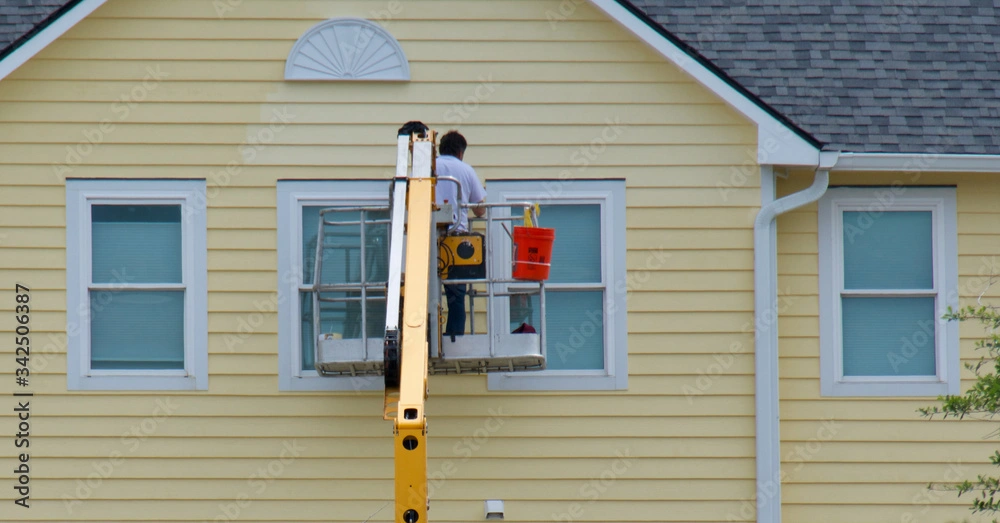 Man updates and replaces yellow siding on a house