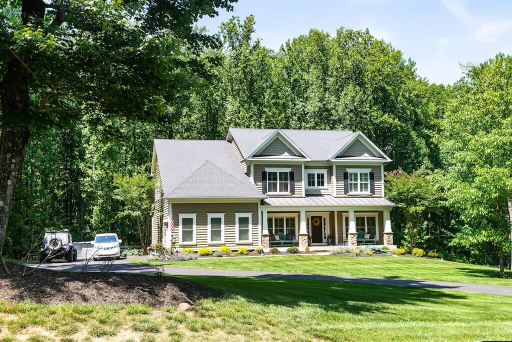 Residential two-story detached house on the edge of the forest with a green lawn in front