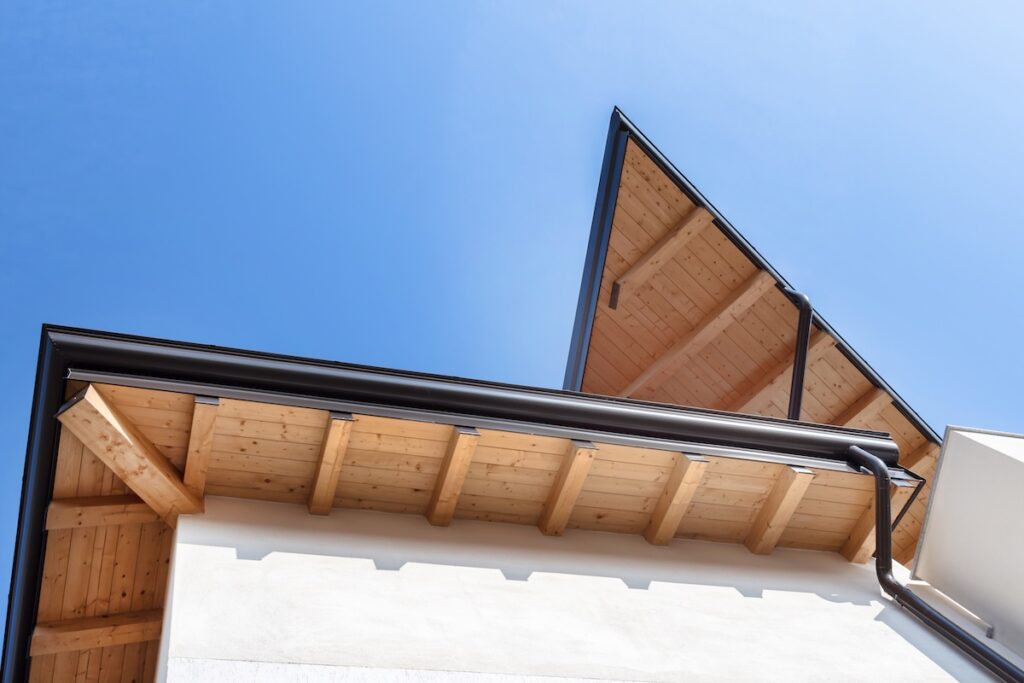 New wooden warm ecological house roof with steel gutter rain system. Professional construction and drainage pipes installation.