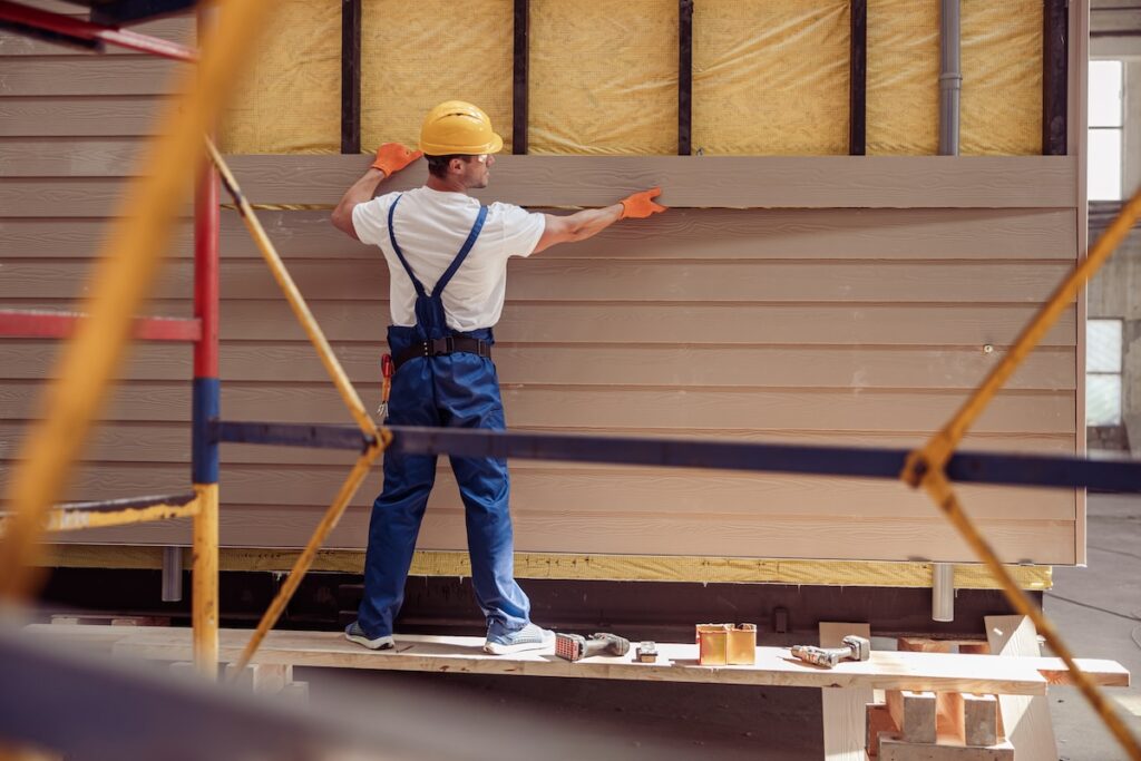 Male roofer installs siding on house