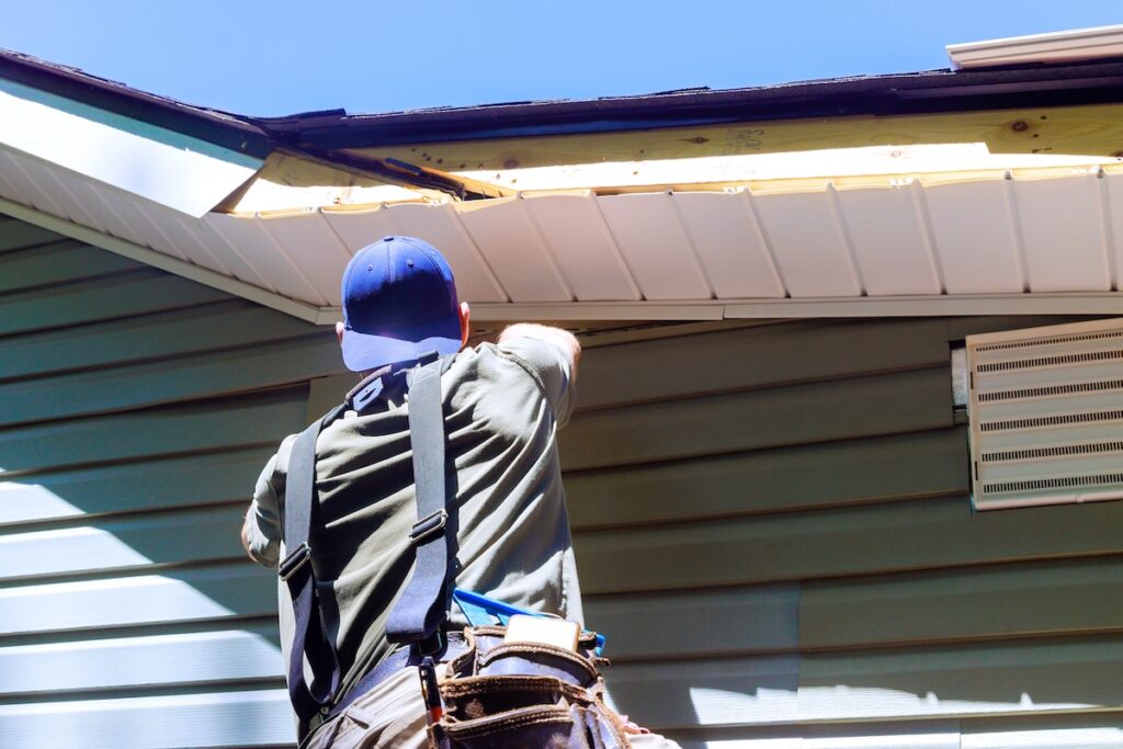 an employee installs vinyl plastic siding panels on wall facade of new home