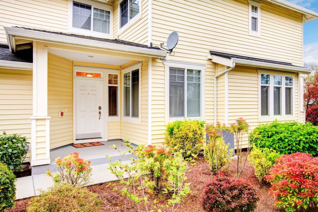 Two story siding house with small porch and front flowerbed, and yellow siding