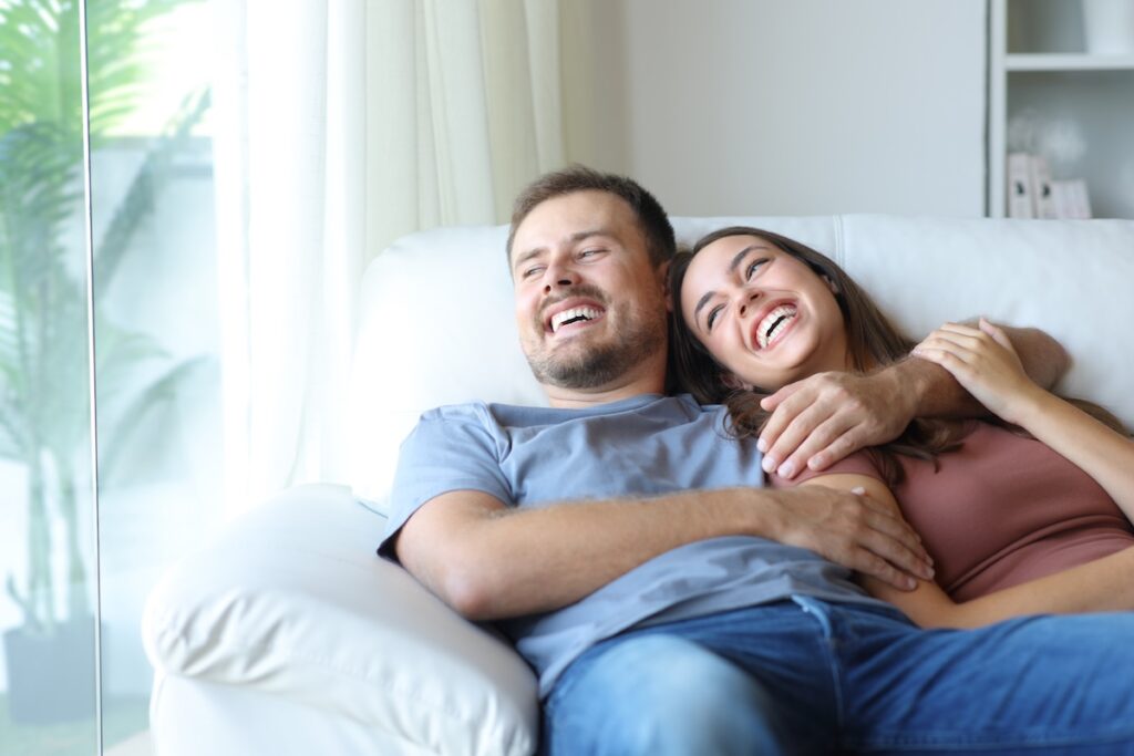couple at home laughing looking through a window