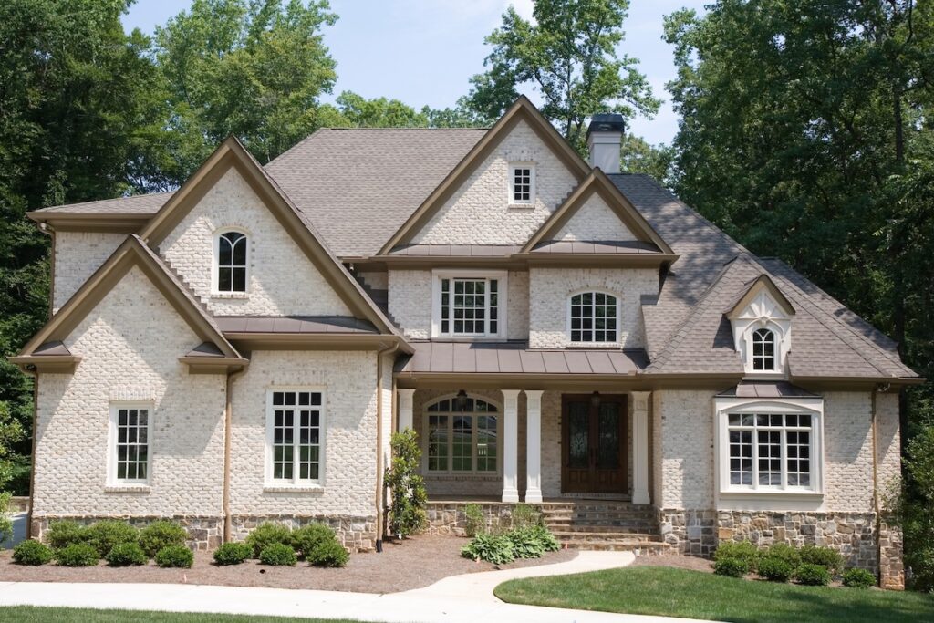 A tan brick house with many gables and roof lines and windows