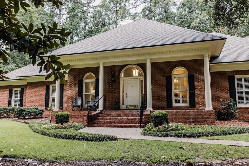 A front side view of an updated red brick ranch traditional house home with off white columns and brick front steps with curb appeal.