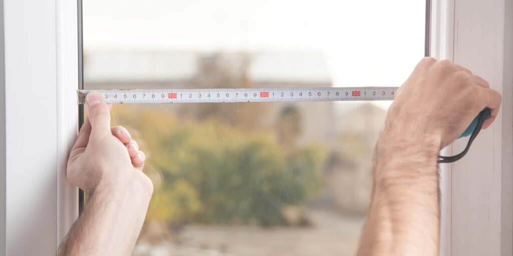 Man measuring window with tape measure