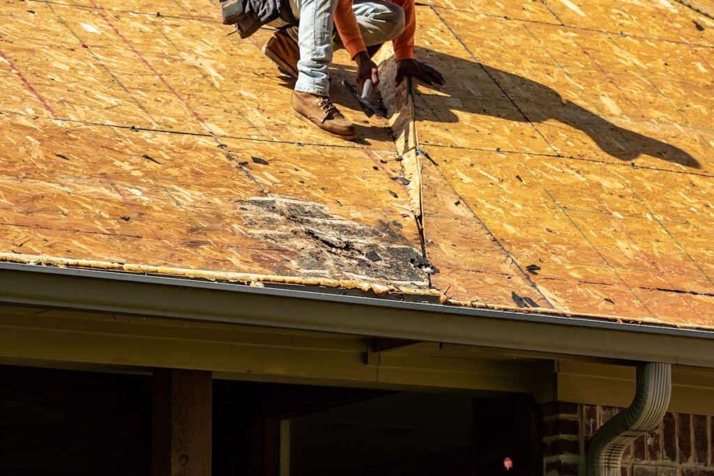 Worker hammers while repairing rotting roof